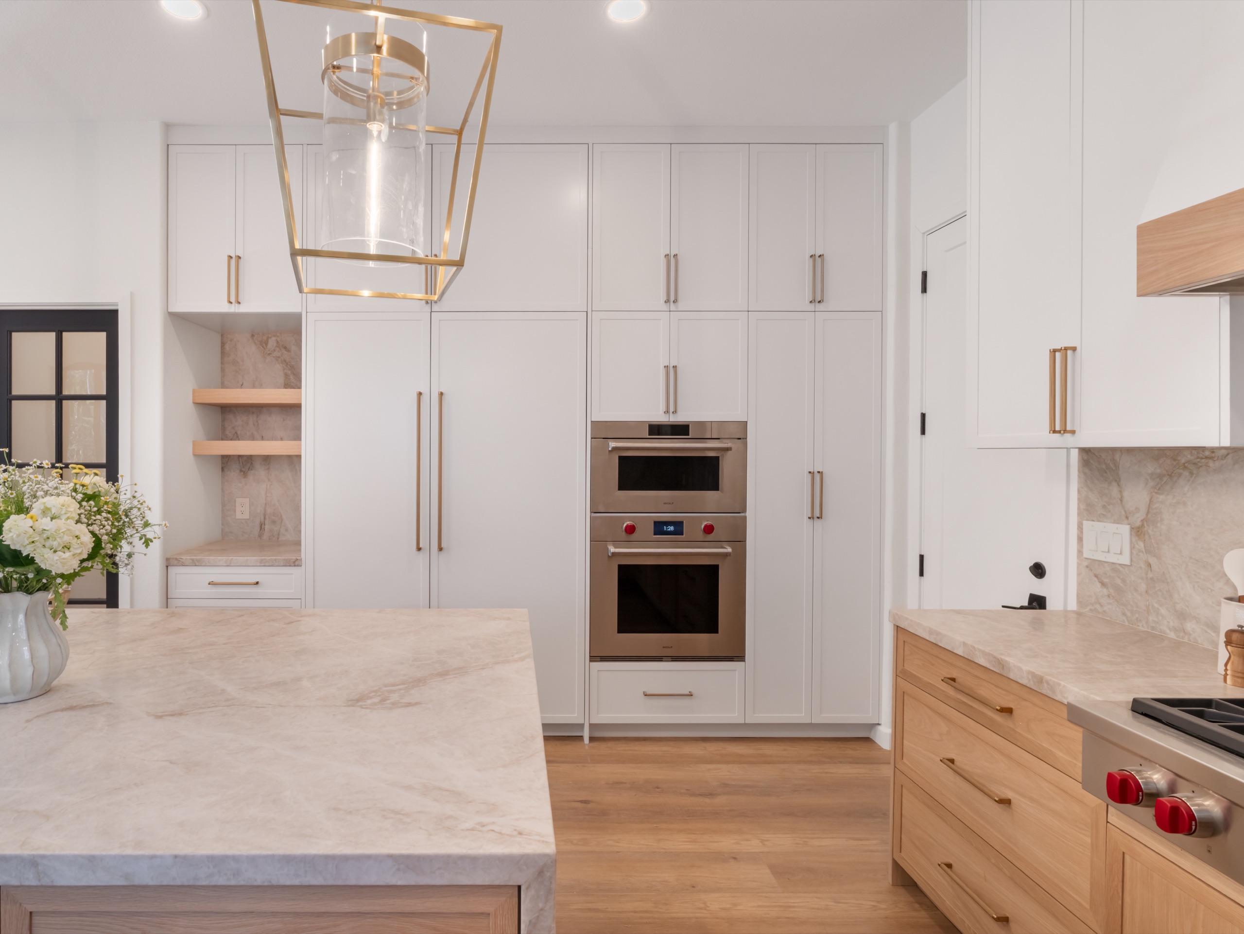 Kitchen with full-height white cabinetry, double ovens, quartzite island and brass lantern
